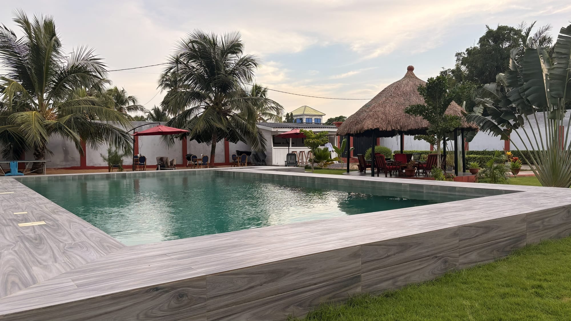 La piscine de Maison Stella entourée de palmiers et de la paillote, au coucher du soleil, à Avepozo (Lomé, Togo)